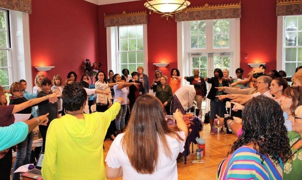 A Group Of People In A Room With Hands Raised.