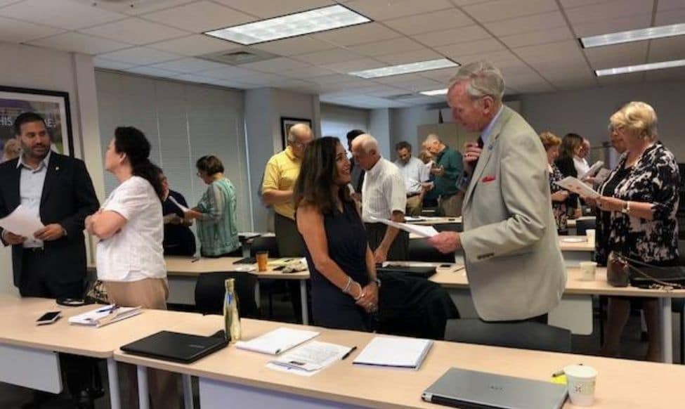 A Group Of People Standing Around A Room.