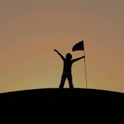 A person standing on top of a hill with their arms in the air.