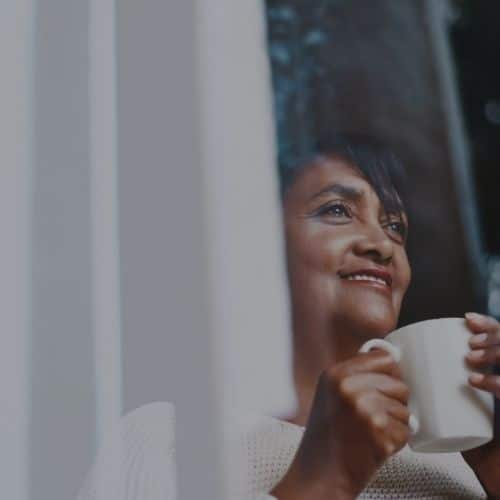 A woman holding a cup looking out of the window.