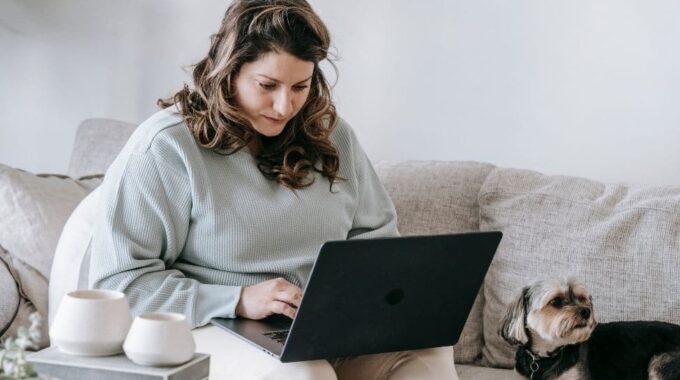 A Woman Sitting On The Couch Looking At Her Laptop.