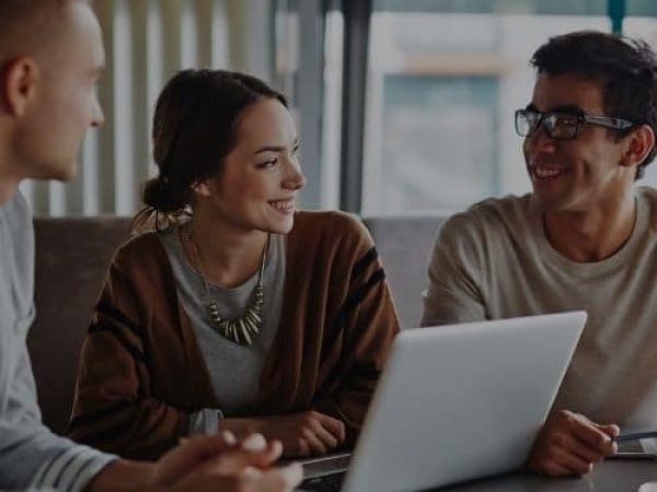 Three people are sitting at a table with a laptop.