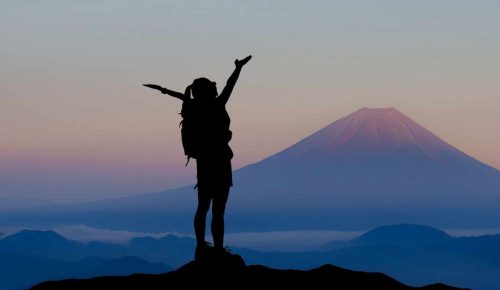 A person standing on top of a hill with their arms up.