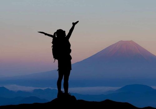 A person standing on top of a hill with their arms up.